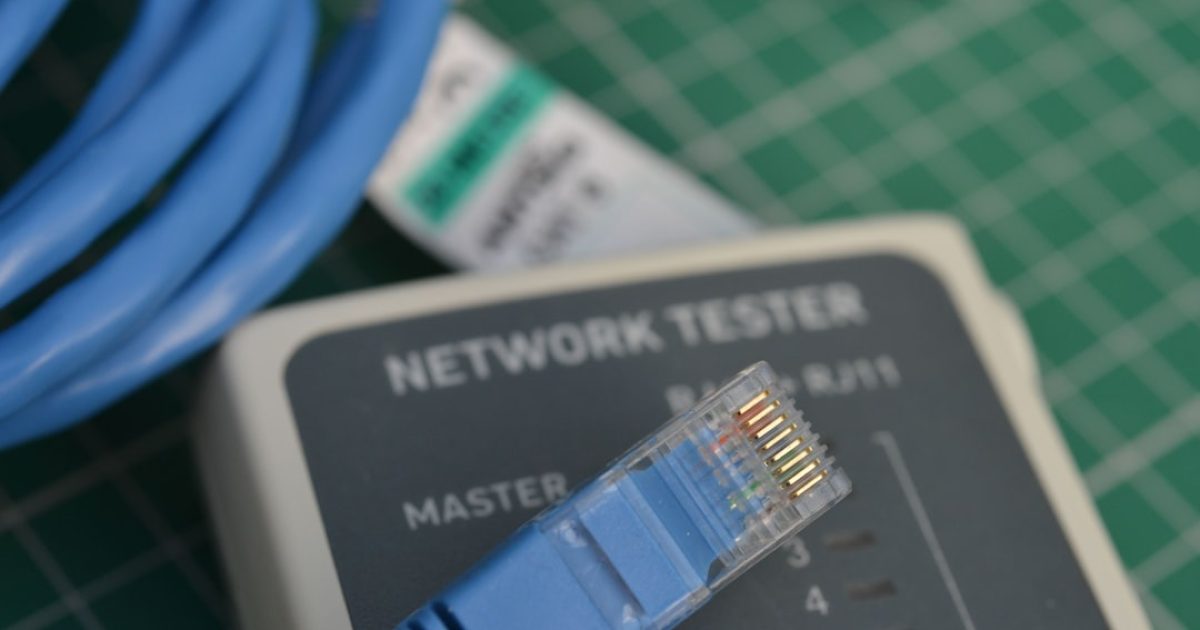 Cabo Ethernet conectado a um portátil ao lado de um router Wi-Fi, simbolizando a comparação entre as duas tecnologias de rede.
